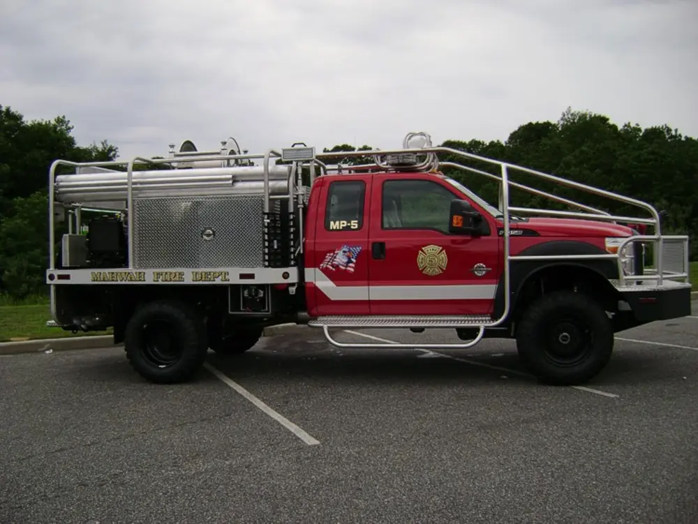 Exterior view of small fire truck showing cab, body compartments, and wheel/tire area.