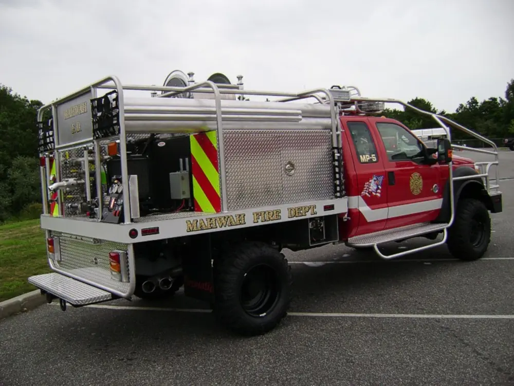 Exterior view of small fire truck showing cab, body compartments, and wheel/tire area.