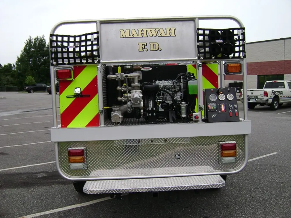 Exterior view of small fire truck showing cab, body compartments, and wheel/tire area.