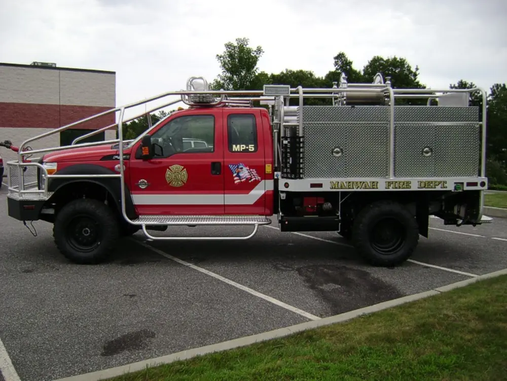 Exterior view of small fire truck showing cab, body compartments, and wheel/tire area.