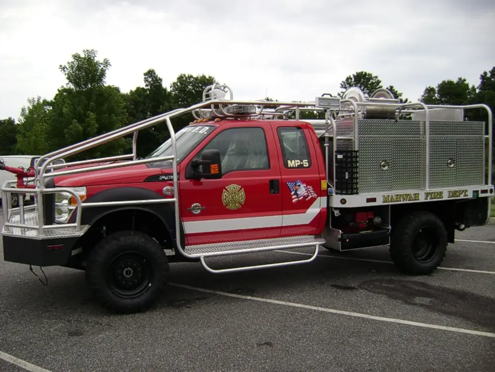 Exterior view of small fire truck showing cab, body compartments, and wheel/tire area.