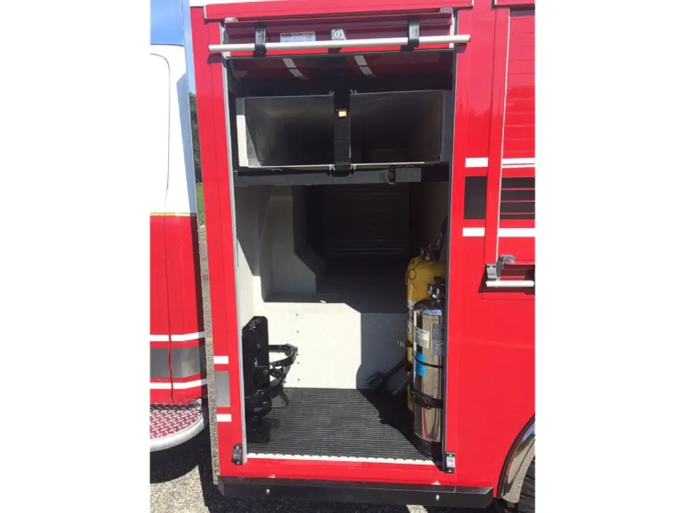 Exterior view of small fire truck showing cab, body compartments, and wheel/tire area.