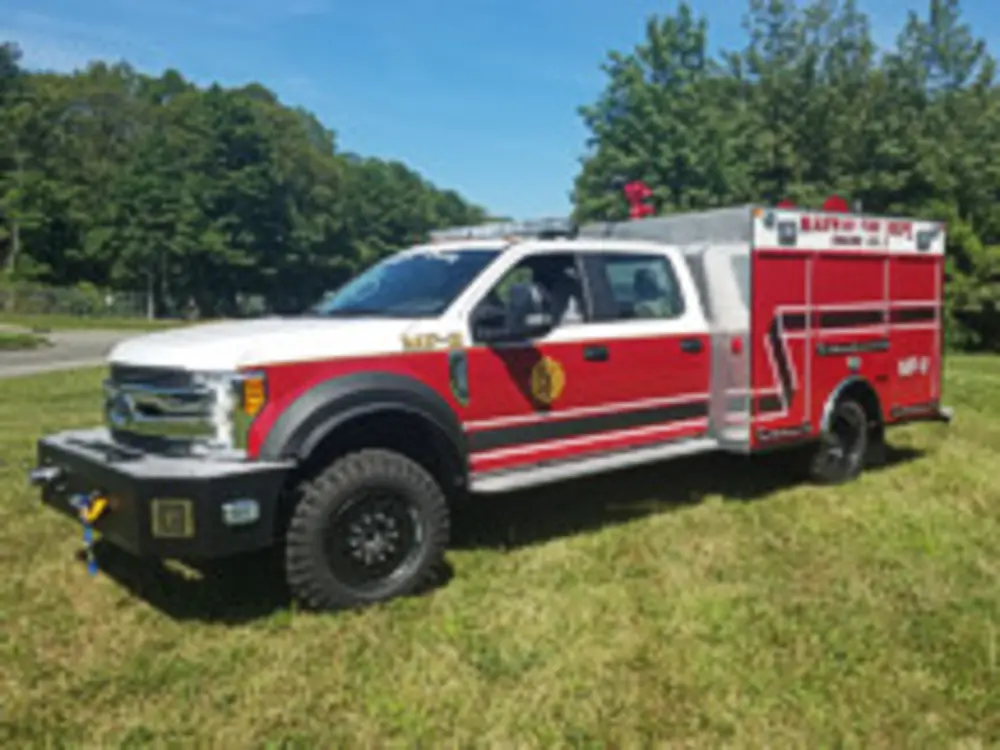 Exterior view of small fire truck showing cab, body compartments, and wheel/tire area.
