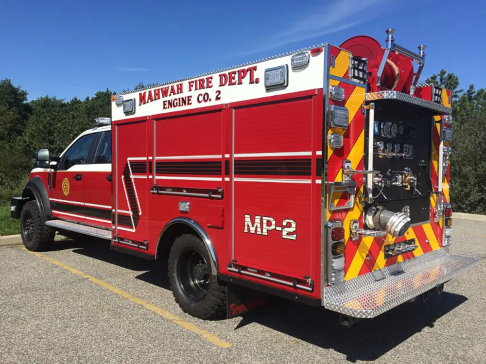 Exterior view of small fire truck showing cab, body compartments, and wheel/tire area.