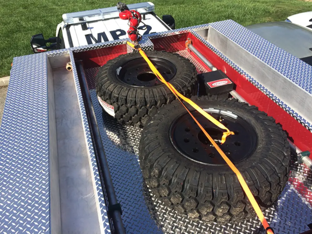 Exterior view of small fire truck showing cab, body compartments, and wheel/tire area.