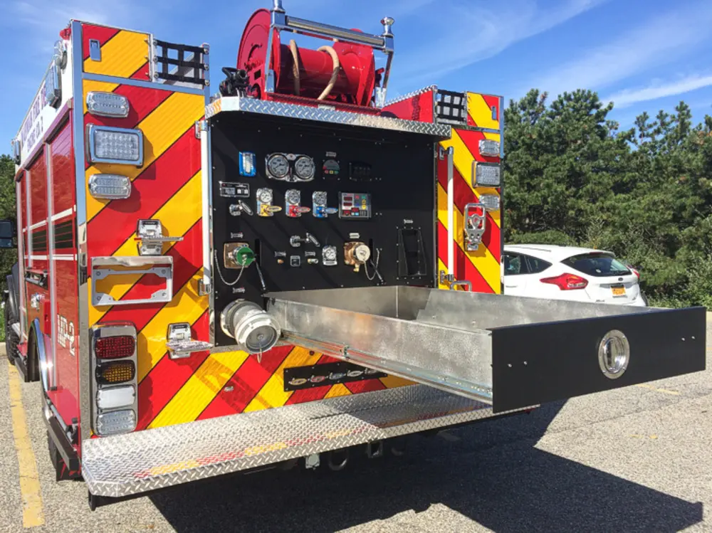 Exterior view of small fire truck showing cab, body compartments, and wheel/tire area.