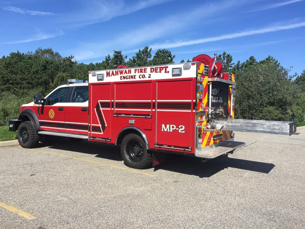 Exterior view of small fire truck showing cab, body compartments, and wheel/tire area.