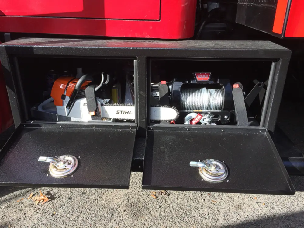 Exterior view of small fire truck showing cab, body compartments, and wheel/tire area.