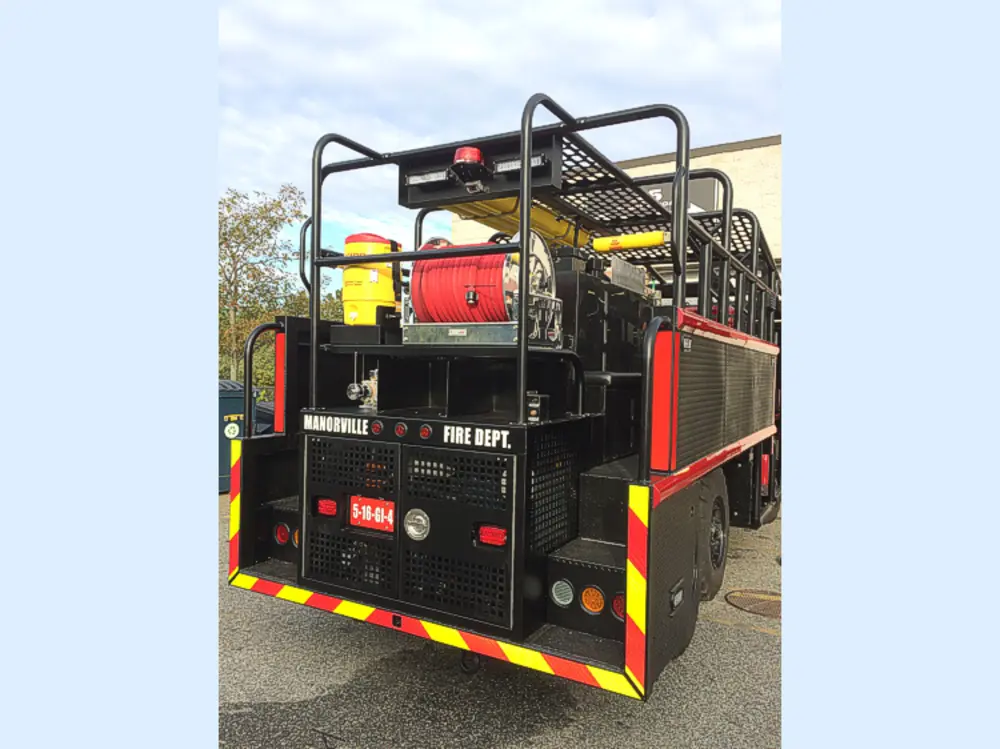 Exterior view of small fire truck showing cab, body compartments, and wheel/tire area.