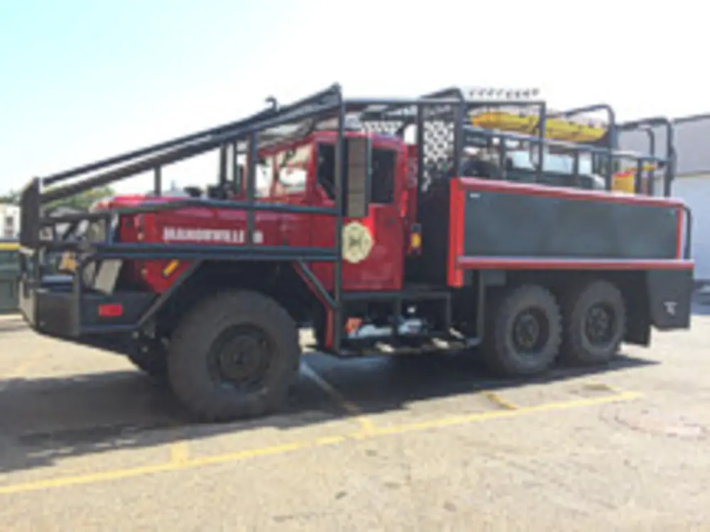 Exterior view of small fire truck showing cab, body compartments, and wheel/tire area.