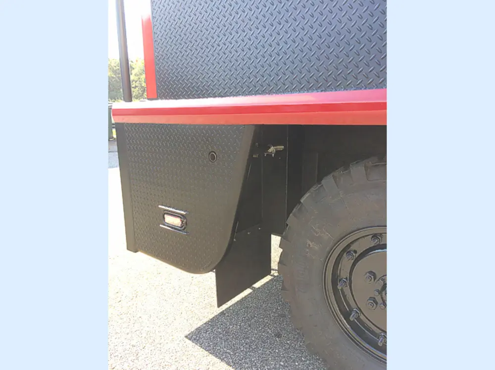 Exterior view of small fire truck showing cab, body compartments, and wheel/tire area.