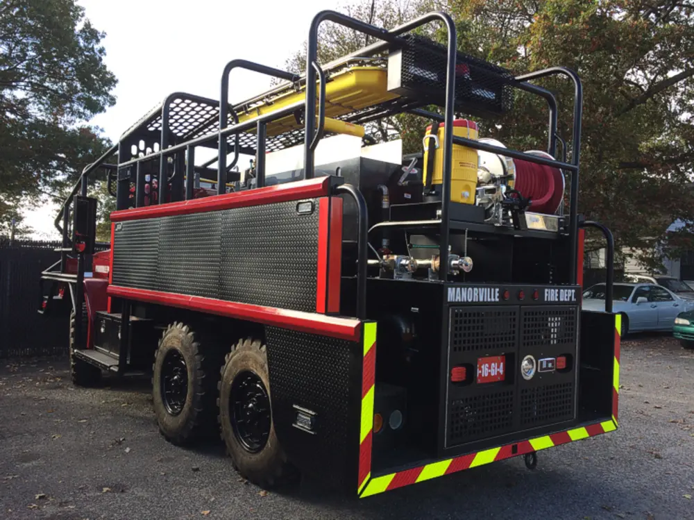 Exterior view of small fire truck showing cab, body compartments, and wheel/tire area.