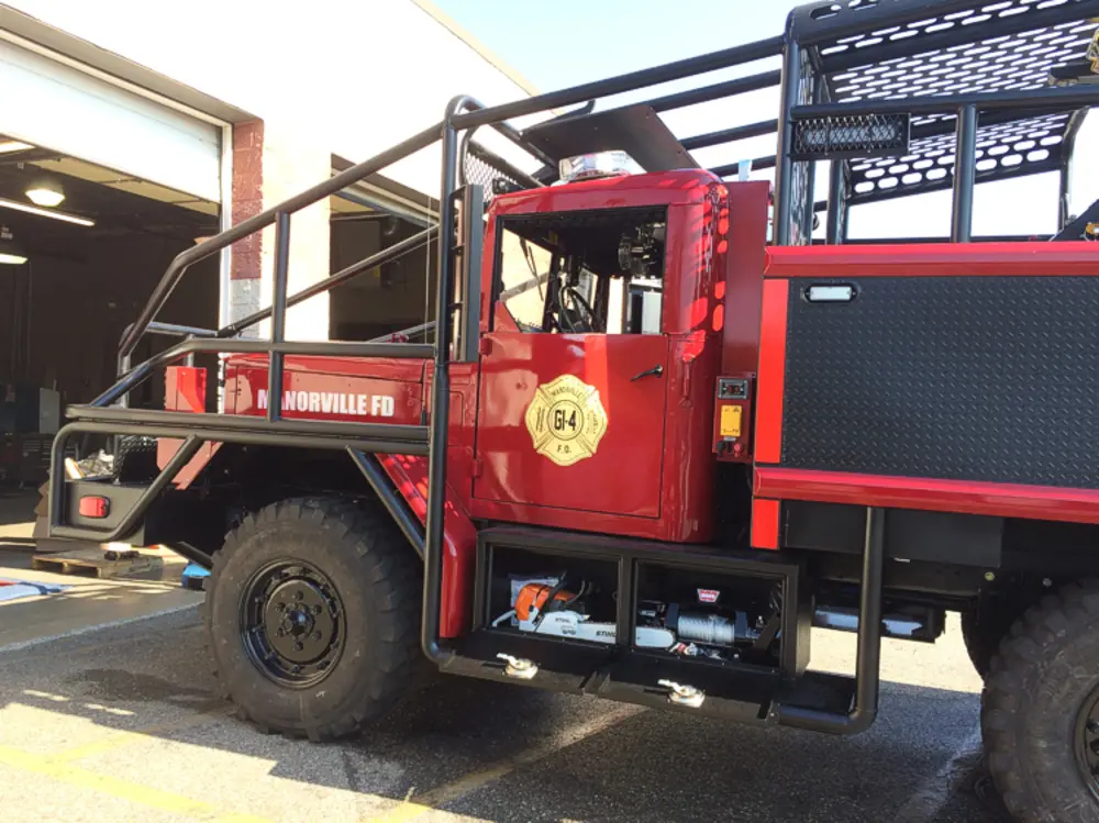 Exterior view of small fire truck showing cab, body compartments, and wheel/tire area.