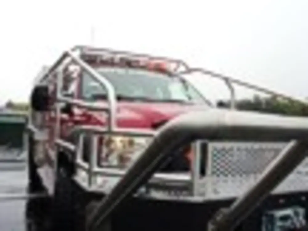 Exterior view of small fire truck showing cab, body compartments, and wheel/tire area.