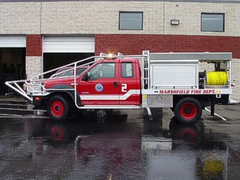 Exterior view of small fire truck showing cab, body compartments, and wheel/tire area.