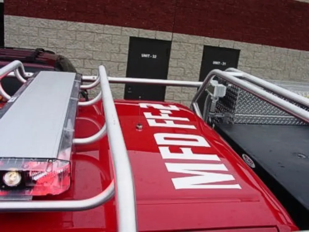 Exterior view of small fire truck showing cab, body compartments, and wheel/tire area.