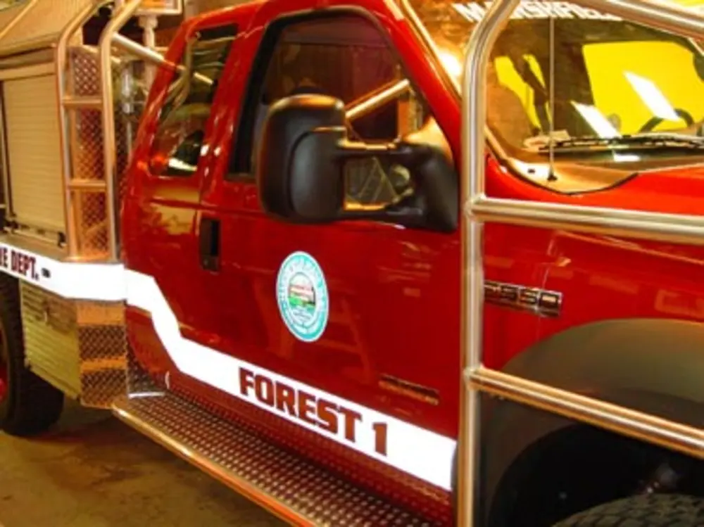 Exterior view of small fire truck showing cab, body compartments, and wheel/tire area.