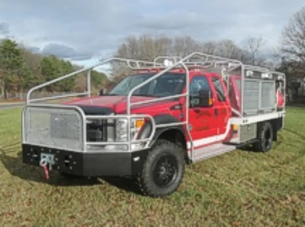 Exterior view of small fire truck showing cab, body compartments, and wheel/tire area.