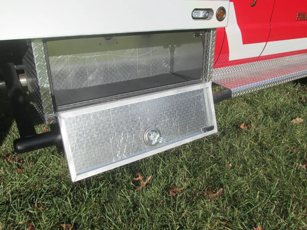 Exterior view of small fire truck showing cab, body compartments, and wheel/tire area.