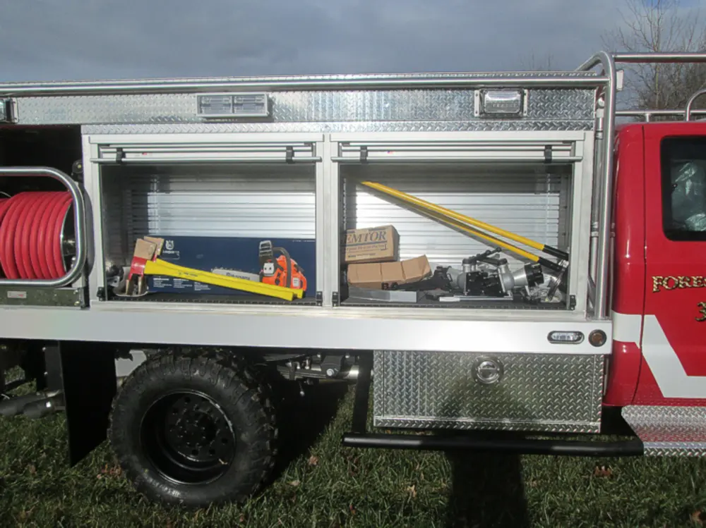 Exterior view of small fire truck showing cab, body compartments, and wheel/tire area.