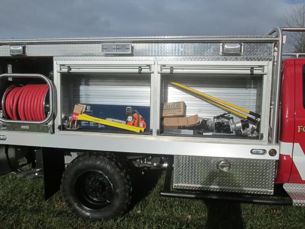 Exterior view of small fire truck showing cab, body compartments, and wheel/tire area.