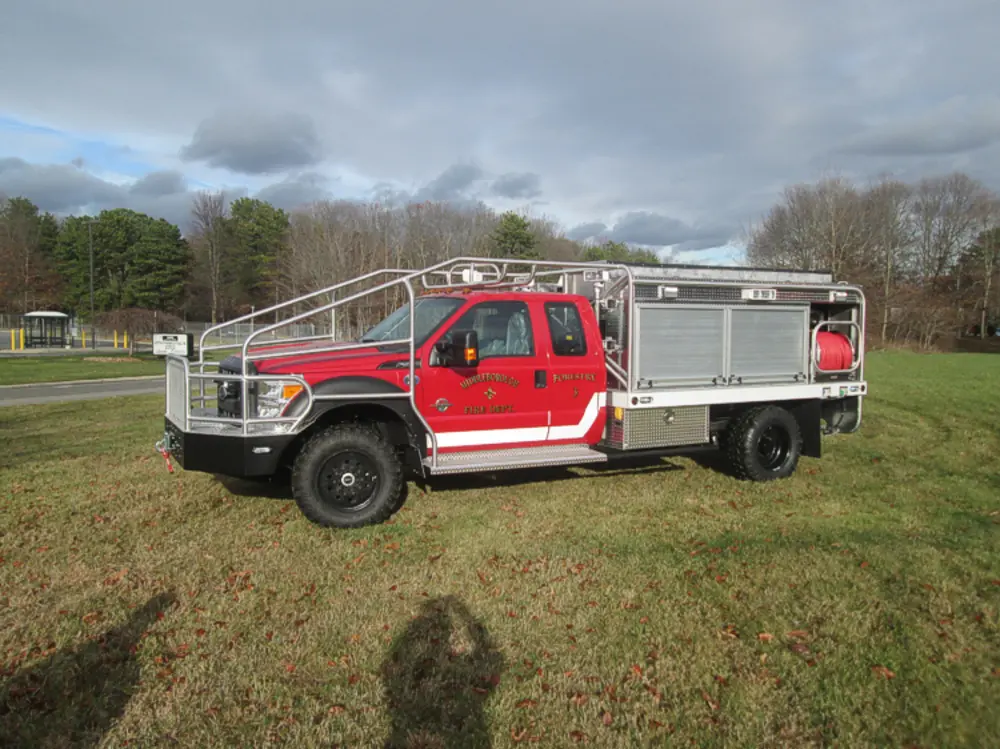 Exterior view of small fire truck showing cab, body compartments, and wheel/tire area.