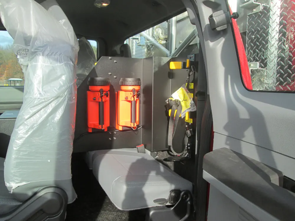Exterior view of small fire truck showing cab, body compartments, and wheel/tire area.