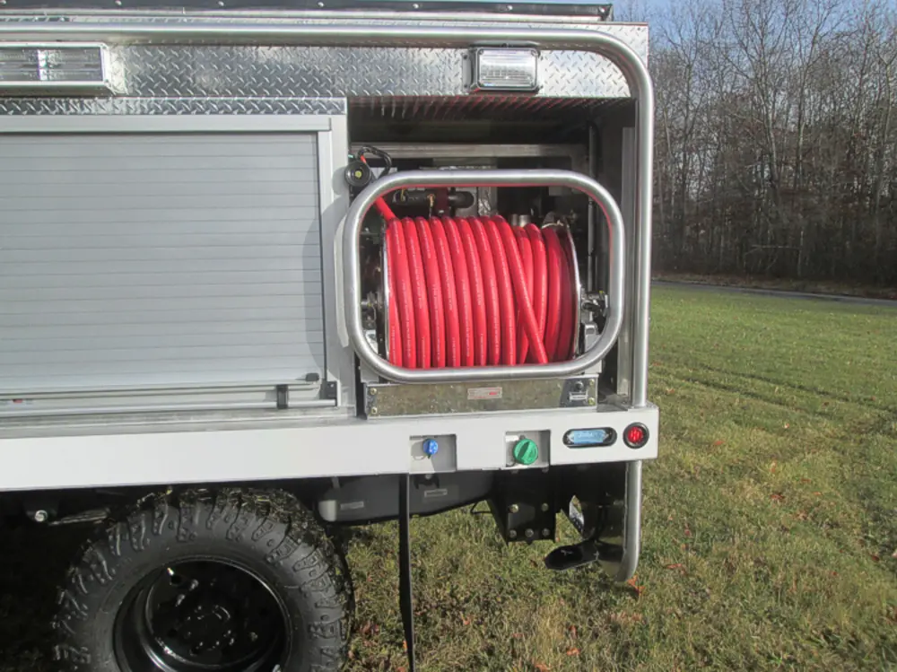Exterior view of small fire truck showing cab, body compartments, and wheel/tire area.