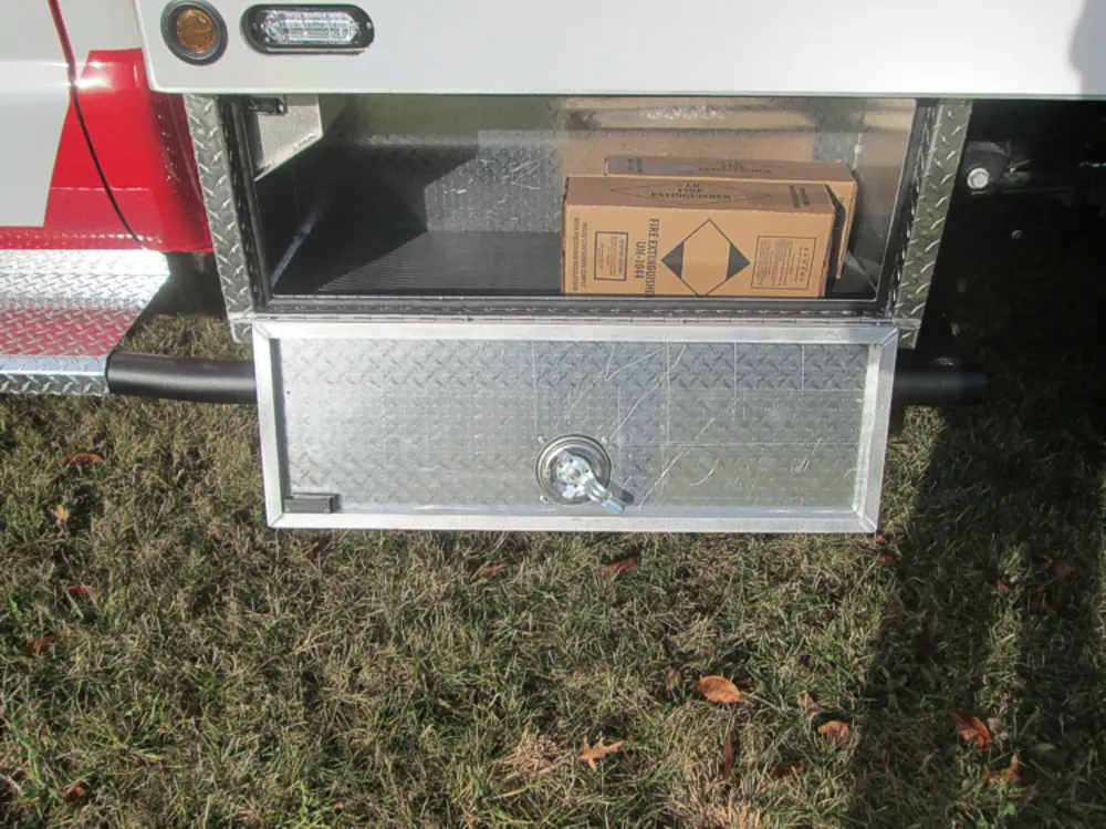 Exterior view of small fire truck showing cab, body compartments, and wheel/tire area.