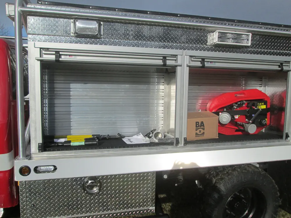 Exterior view of small fire truck showing cab, body compartments, and wheel/tire area.