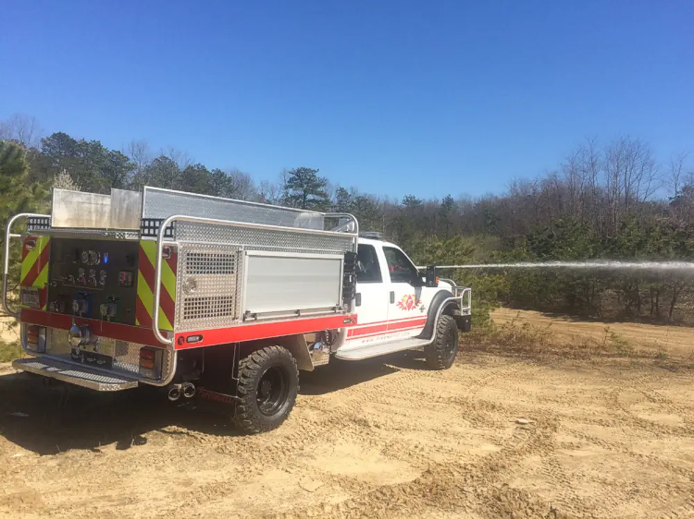 Exterior view of small fire truck showing cab, body compartments, and wheel/tire area.