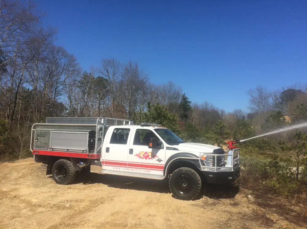 Exterior view of small fire truck showing cab, body compartments, and wheel/tire area.