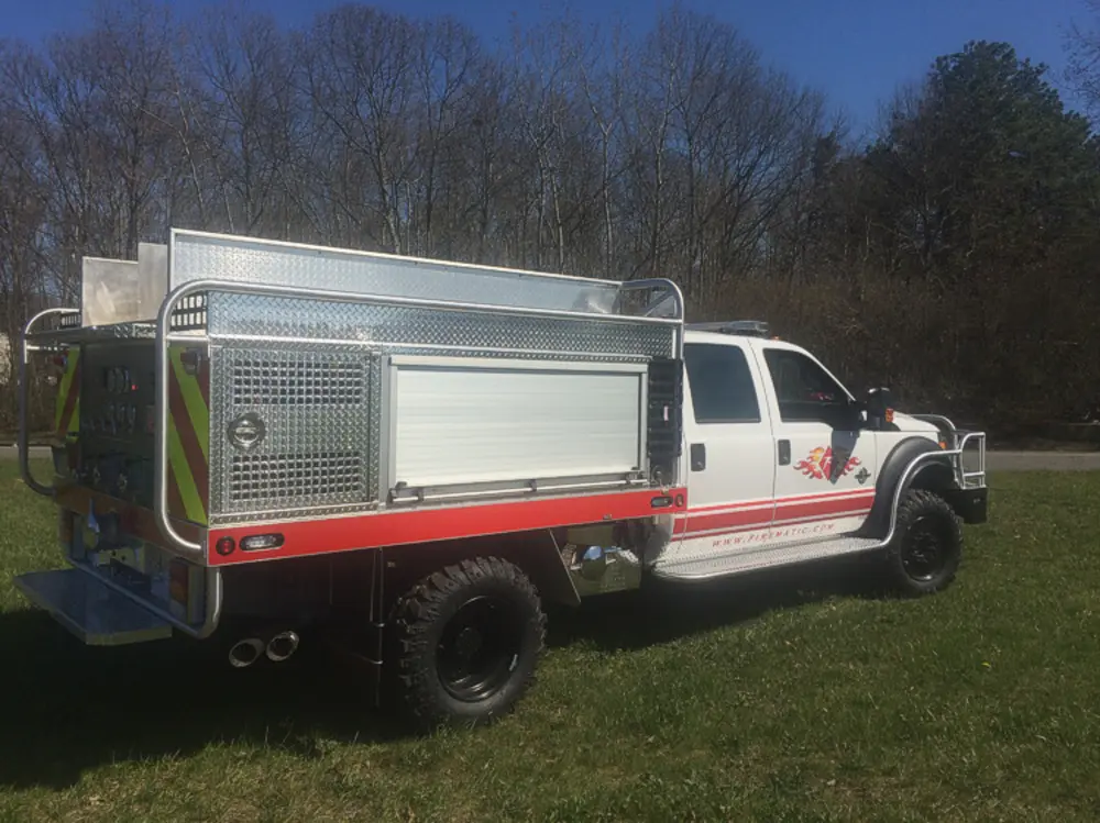 Exterior view of small fire truck showing cab, body compartments, and wheel/tire area.