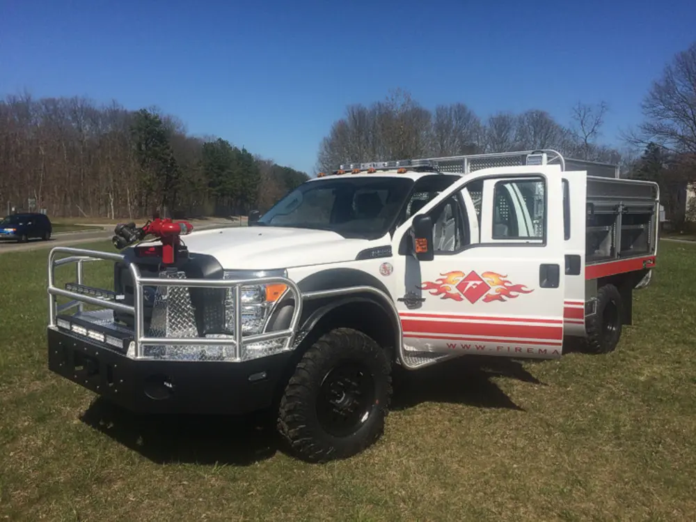 Exterior view of small fire truck showing cab, body compartments, and wheel/tire area.