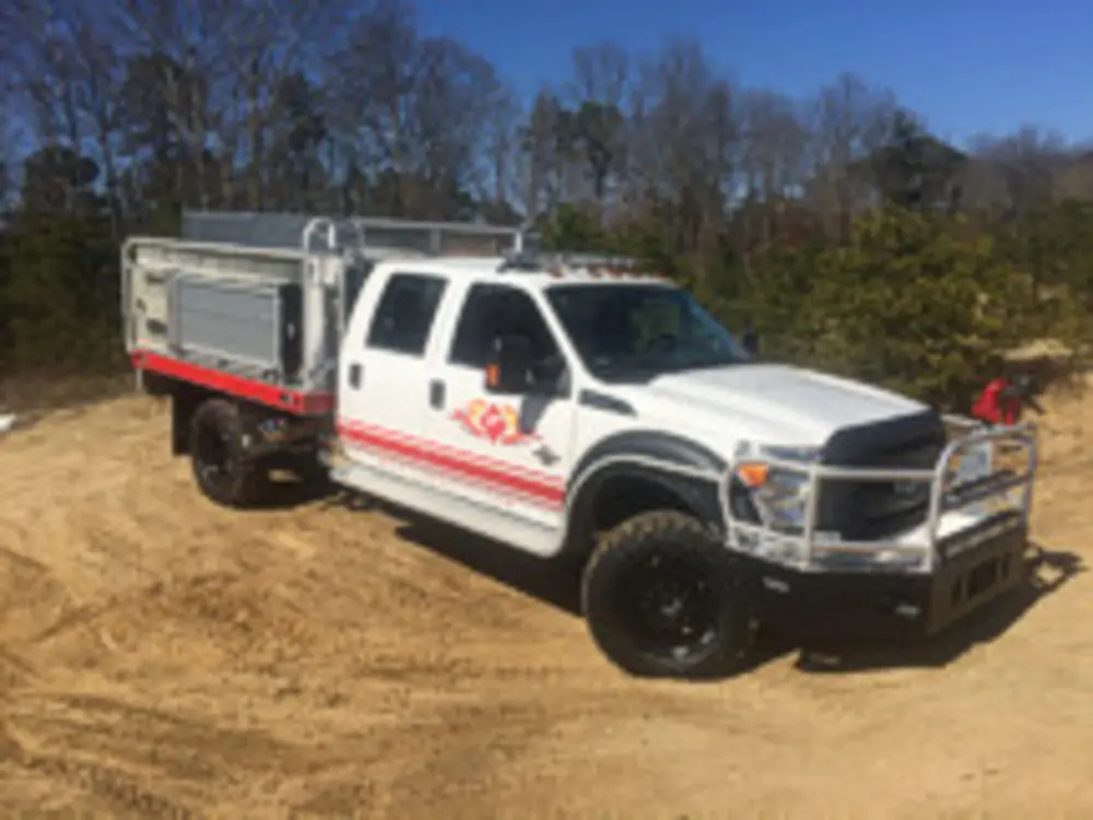 Exterior view of small fire truck showing cab, body compartments, and wheel/tire area.