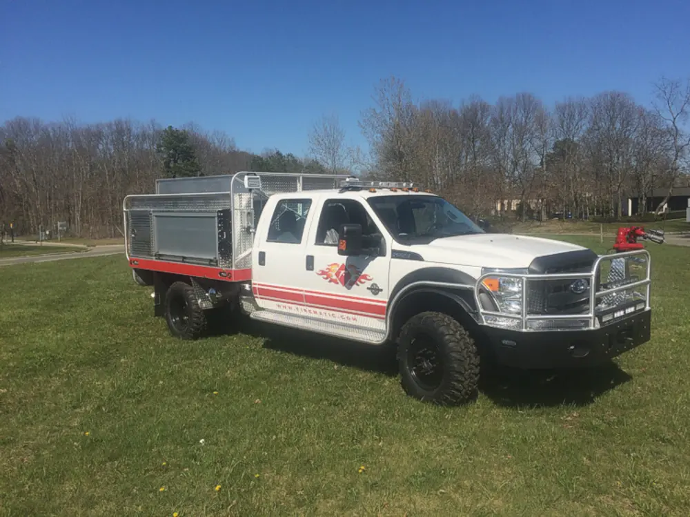 Exterior view of small fire truck showing cab, body compartments, and wheel/tire area.