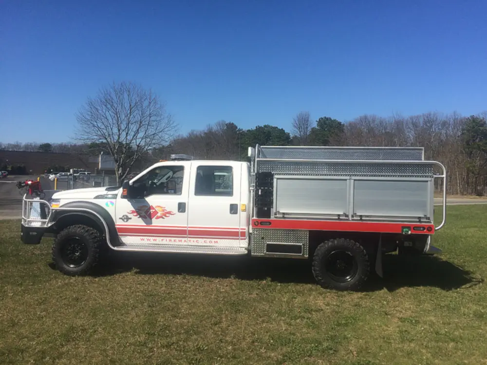 Exterior view of small fire truck showing cab, body compartments, and wheel/tire area.