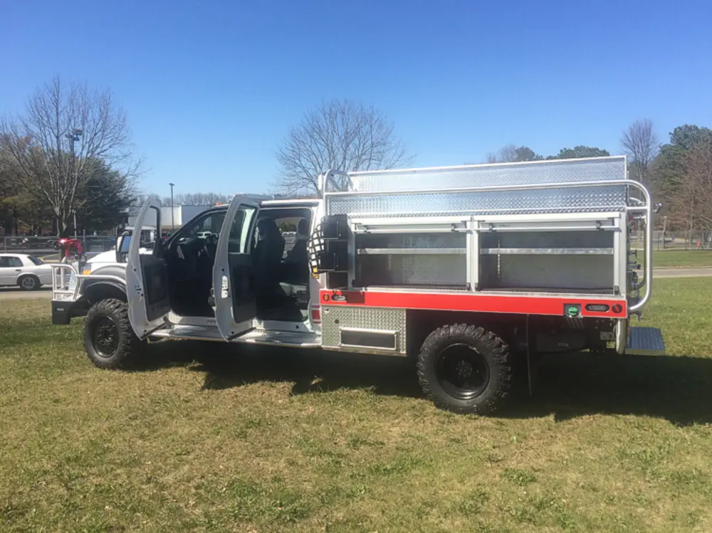 Exterior view of small fire truck showing cab, body compartments, and wheel/tire area.