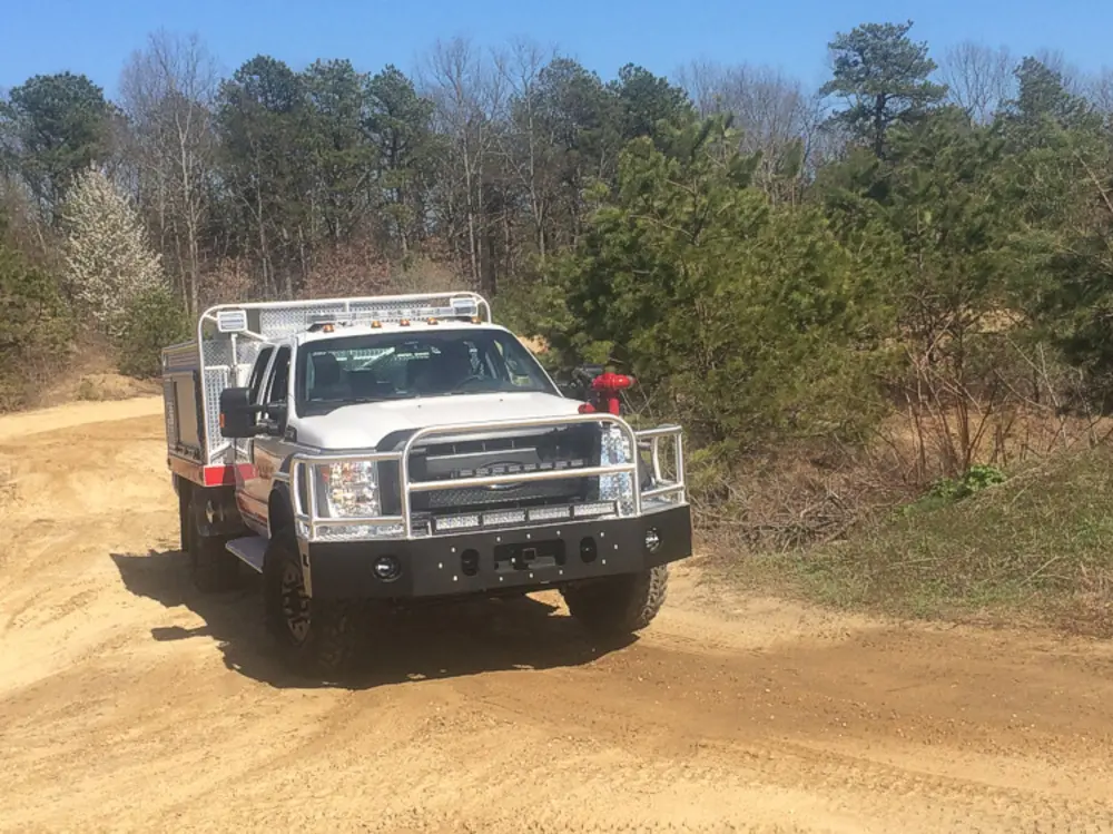 Exterior view of small fire truck showing cab, body compartments, and wheel/tire area.