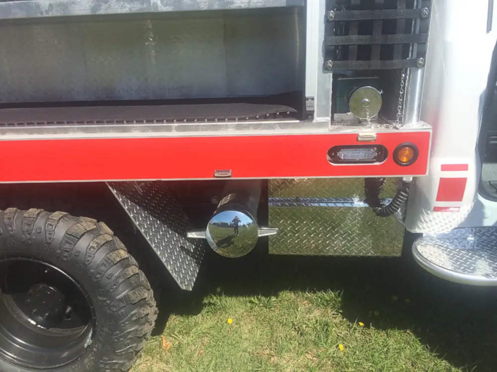 Exterior view of small fire truck showing cab, body compartments, and wheel/tire area.
