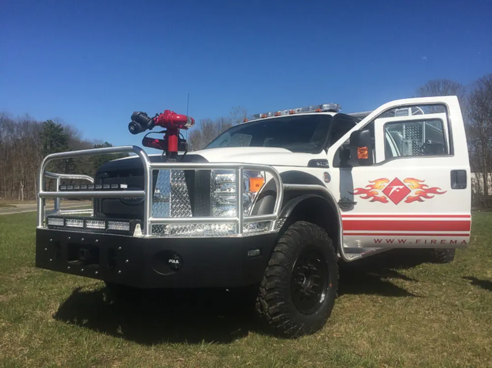Exterior view of small fire truck showing cab, body compartments, and wheel/tire area.