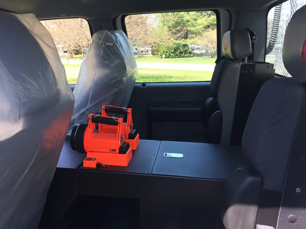 Exterior view of small fire truck showing cab, body compartments, and wheel/tire area.