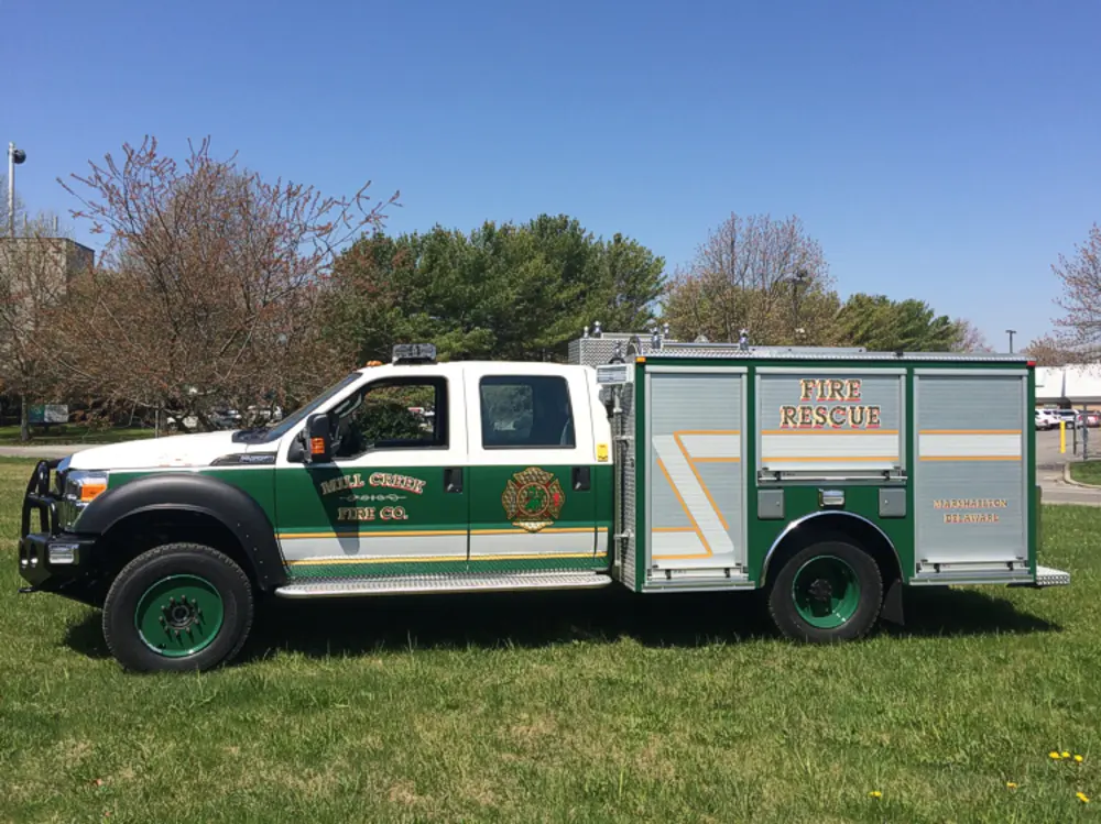 Exterior view of small fire truck showing cab, body compartments, and wheel/tire area.