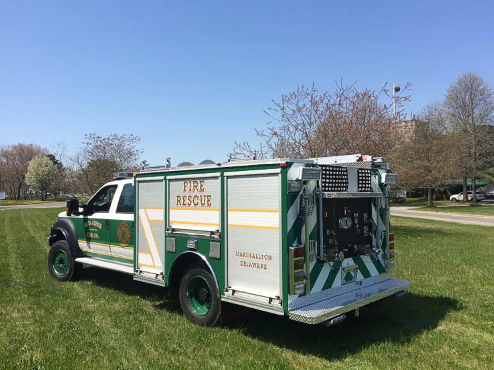 Exterior view of small fire truck showing cab, body compartments, and wheel/tire area.