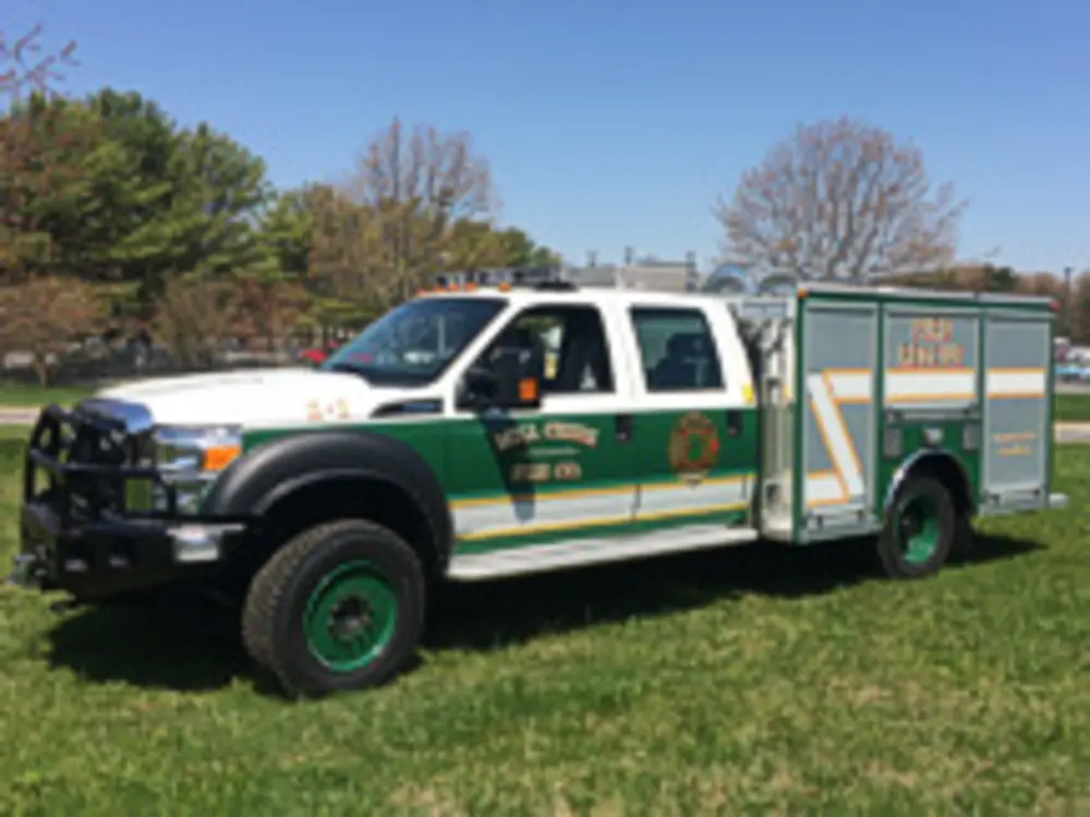 Exterior view of small fire truck showing cab, body compartments, and wheel/tire area.