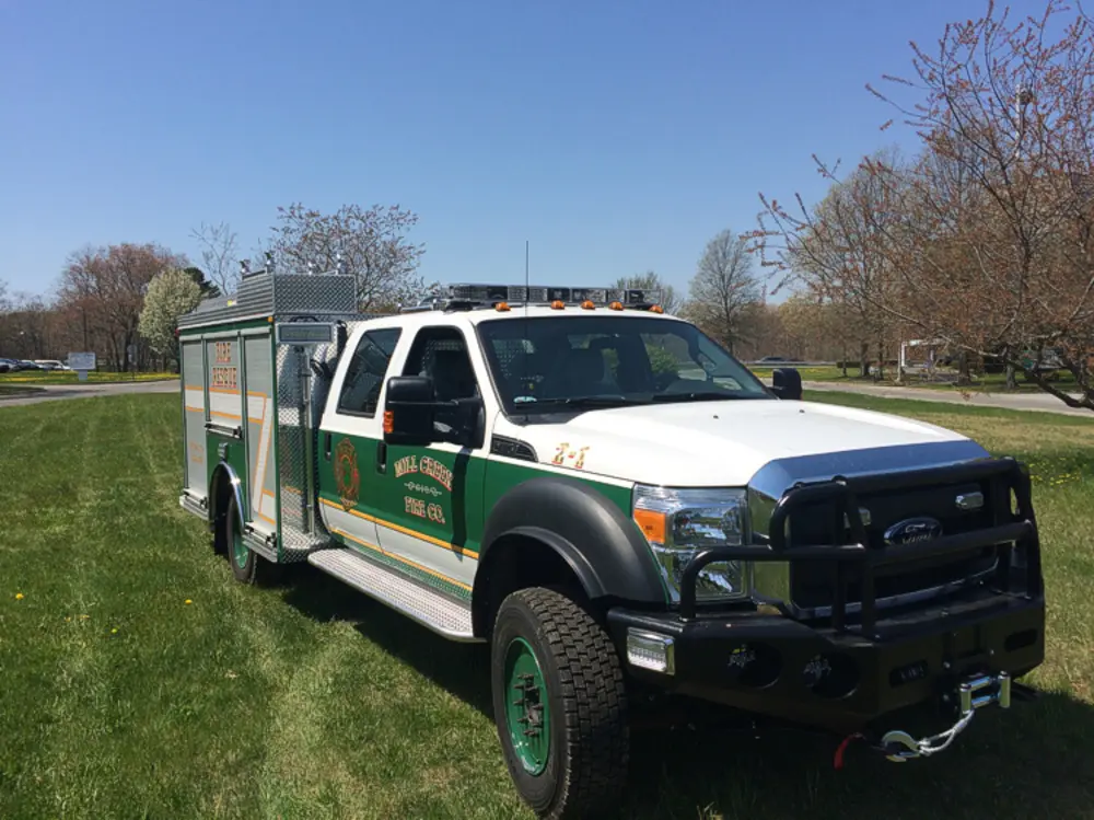 Exterior view of small fire truck showing cab, body compartments, and wheel/tire area.