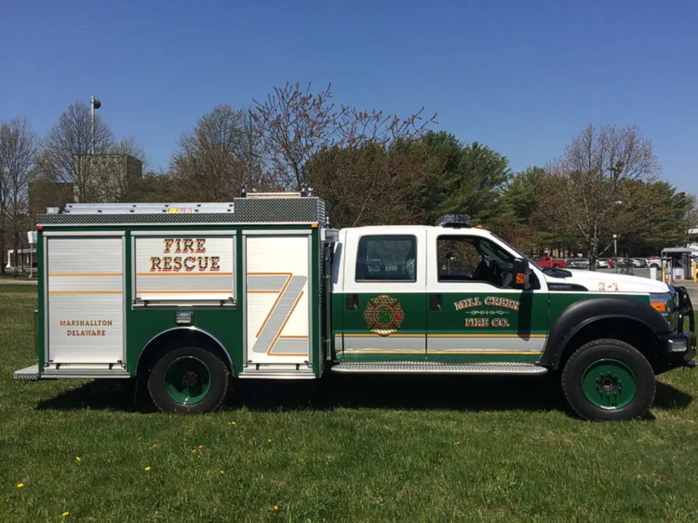 Exterior view of small fire truck showing cab, body compartments, and wheel/tire area.