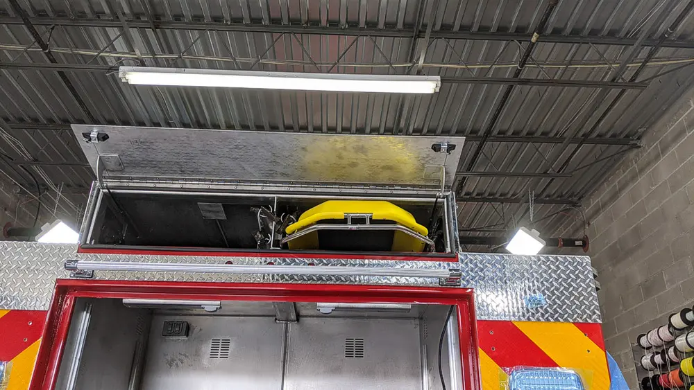 Exterior view of small fire truck showing cab, body compartments, and wheel/tire area.