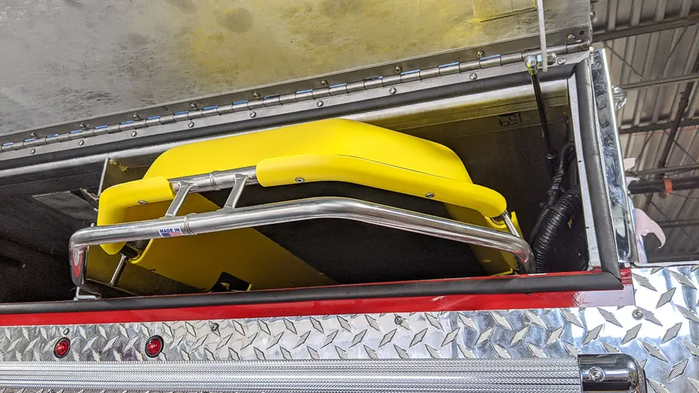 Exterior view of small fire truck showing cab, body compartments, and wheel/tire area.