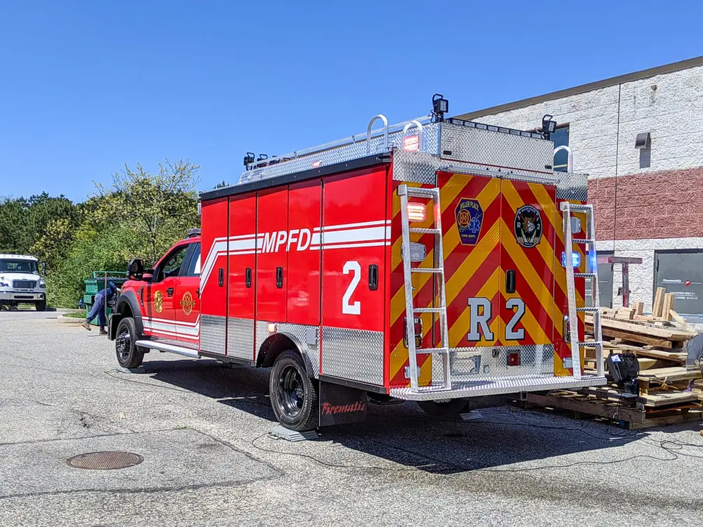 Exterior view of small fire truck showing cab, body compartments, and wheel/tire area.